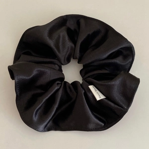 Close-up of black satin scrunchie with handmade tag showing smooth glossy texture
