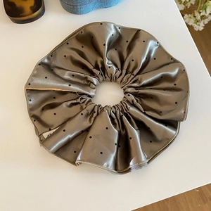 Detail of a bronze satin scrunchie with black polka dots on a minimalist white desk