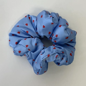 Detailaufnahme des hellblauen Satin-Scrunchies mit roten Herzen und weichen Falten