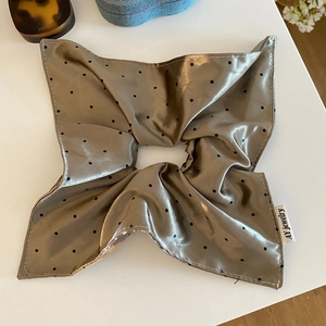 Close-up of olive green satin scrunchie with black polka dots and branded textile label