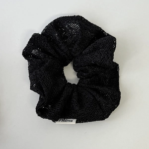 Détail d'un chouchou en dentelle noire avec texture florale et étiquette de marque