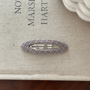 Close-up of a blue and brown plaid fabric hair clip on a natural linen background