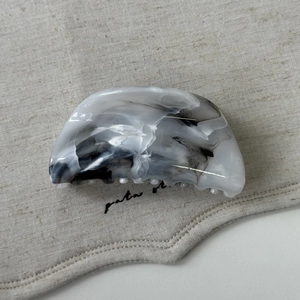 Gros plan d'une pince à cheveux motif marbre gris sur un tissu en lin beige