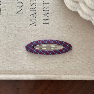 Close-up of red and blue plaid fabric oval BB hair clip on a textured notebook