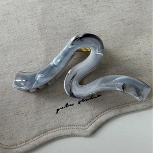 Détail d'une pince à cheveux marbrée avec forme en S et ressort métallique doré