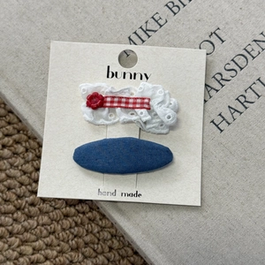 Detail of denim heart hair clip and white lace bow with red button on a branded card