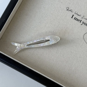 Detail of fish-shaped acetate hair clip with pearlescent white resin and metal duckbill grip