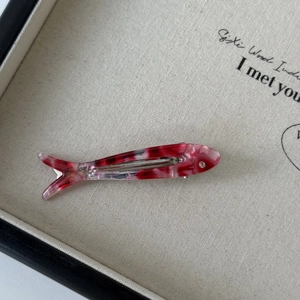 Detailed close-up of fish-shaped acetate hair clip with pink marble texture and crystal eye