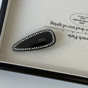 Detail of a black drop-shaped barrette with colorful rhinestones and gold French lettering