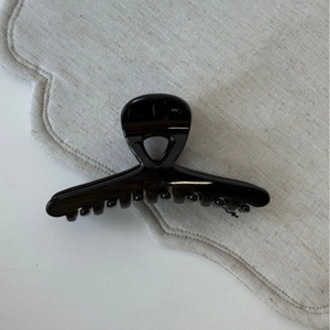 Gros plan d'une pince à cheveux noire brillante minimaliste sur tissu en lin