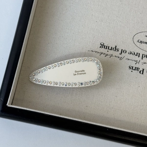 Detail of a vintage cream white drop-shaped hair clip with sparkling rhinestones and gold text