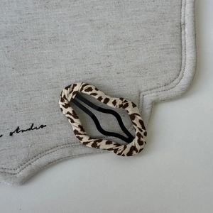 Macro shot of leopard print fabric covered drop-shaped metal BB hair clip with studio prop