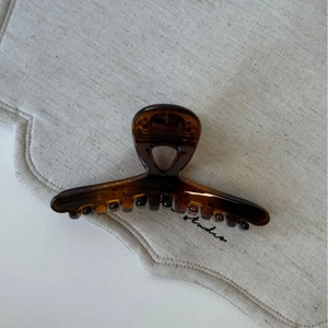 Détail de la pince à cheveux écaille ambrée sur tissu beige montrant la texture brillante