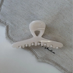 Détail d'une pince à cheveux beige crème brillante sur fond en lin neutre au studio