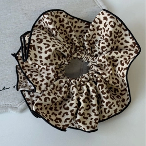 Close-up of leopard print scrunchie with black edging on grey linen background