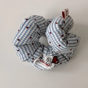 Close-up of blue plaid scrunchie with red hearts and embroidered Ruru patch detail