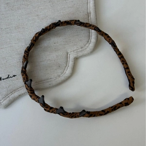 Detail showing leopard print headband with small black hair clips on a fabric base