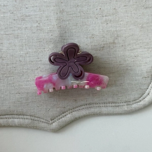 Détail d'une pince à cheveux rose marbré avec une fleur violette sur lin gris clair