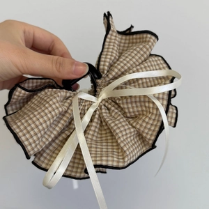 Detail view of the brown plaid fabric hair claw clip with a cream satin bow design