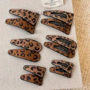 Detail view of leopard print hair clips with white stitching on beige linen background