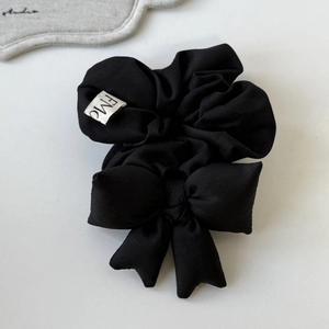 Minimalist black fabric bow scrunchie with a white FMC woven label on plain background