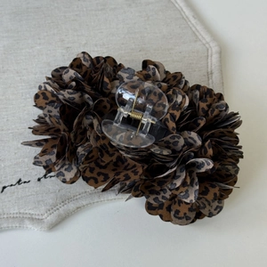 Detail of leopard print fabric flower hair claw clip on a textured beige fabric background