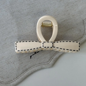 Close-up of a cream bow-shaped hair claw clip with black dotted edges on grey linen