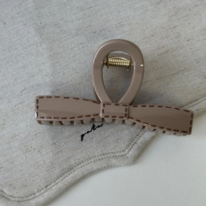 Minimalist beige bow hair claw clip with stitch patterns on neutral fabric texture