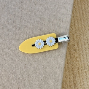 Gros plan sur une pince à cheveux en résine jaune avec deux breloques marguerites en 3D