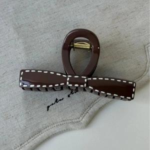 Detail of a dark brown bow hair claw clip with white stitching on linen background