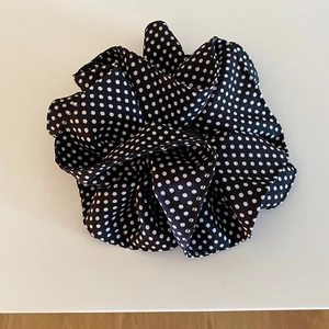 Detailed view of large black and white polka dot scrunchie with soft pleated fabric texture