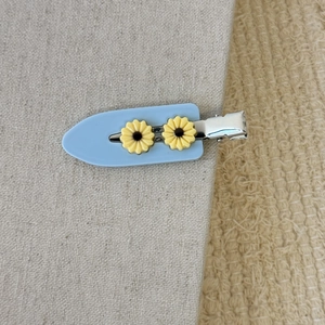 Gros plan d'une barrette en acétate bleu clair avec motifs floraux jaunes et pince canard