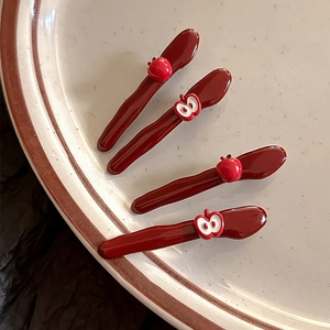 Set of four glossy red apple hair clips in duckbill style displayed on a ceramic plate