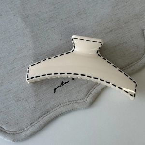 Detailed view of cream hair claw clip with black stitched edges on minimalist linen background
