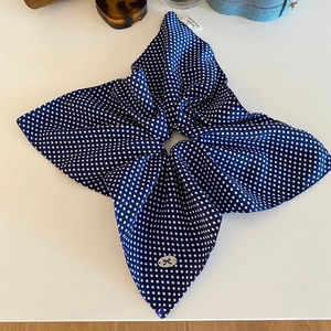 Close-up of navy polka dot satin hair scrunchie with handmade tag and silver bow charm