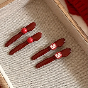Close-up of four red apple-shaped hair clips in a wooden tray with knitting details