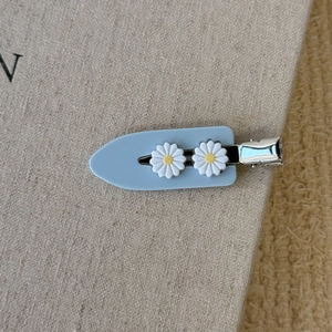 Détail d'une pince à cheveux en acétate bleu clair ornée de deux marguerites blanches