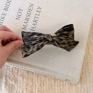 Retro leopard print bow hair clip with gold logo plate on a vintage book background