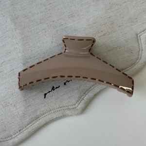 Detail of milk coffee hair claw with brown stitch pattern on beige linen cloth