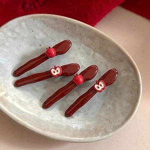 Set of four dark red apple hair clips on a ceramic tray with red knit background