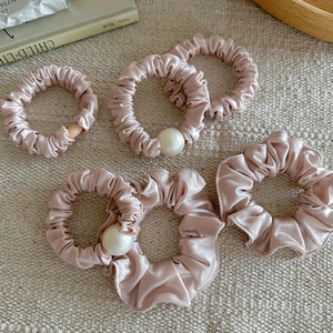 Lot de chouchous en satin rose avec perles élégantes sur fond beige texturé
