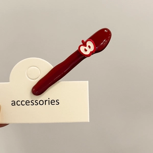 Detail of a burgundy hair clip with a 3D apple motif on a cream-colored display card