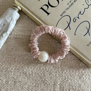 Chouchou élégant en satin de soie rose avec grande perle blanche sur fond texturé
