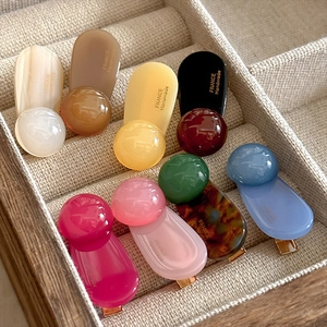 Set mit minimalistischen Haarclips aus Acryl in neun Farben auf einem beigen Kissen