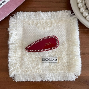 Détail d'une barrette goutte rouge ornée de cristaux sur un support tressé