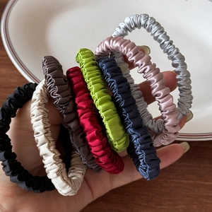 Set of eight silk-like elastic hair scrunchies in multiple colors on a ceramic plate