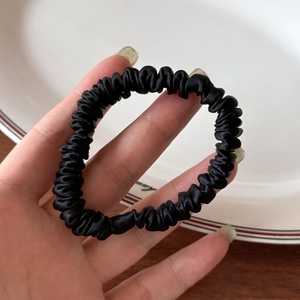 Elegant black silk scrunchie with soft sheen and high elasticity held in hand over a tray