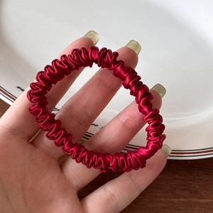 Close-up of deep red silk satin hair scrunchie showing smooth texture and elegant pleats