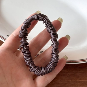 Close-up of a high-elastic silk scrunchie in dark coffee satin with fine pleated texture