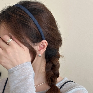 Detailed view of denim headband with silver spiral earrings and a pearl necklace on a model
